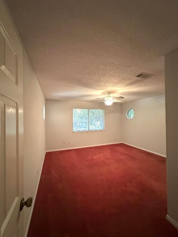 unfurnished room with dark colored carpet, visible vents, baseboards, and ceiling fan