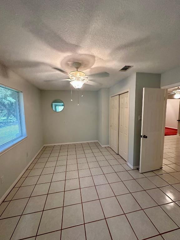 unfurnished bedroom with a closet, a textured ceiling, visible vents, and light tile patterned floors