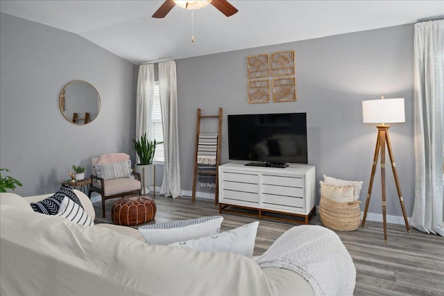 living area featuring lofted ceiling, wood finished floors, baseboards, and ceiling fan