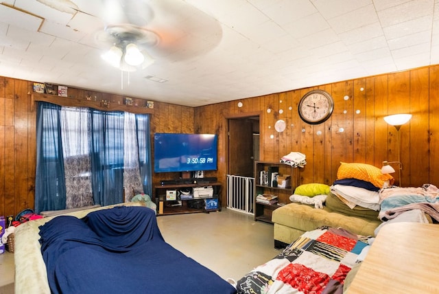 living room featuring wood walls, concrete flooring, ceiling fan, and visible vents