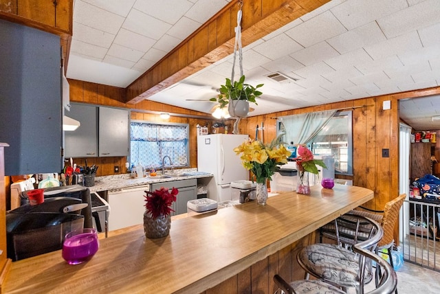 kitchen featuring a sink, ceiling fan, wood walls, visible vents, and freestanding refrigerator