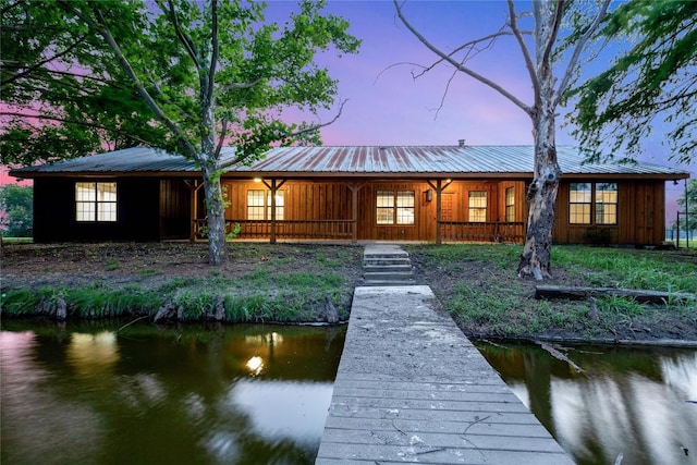 back of property at dusk featuring covered porch, a water view, and metal roof