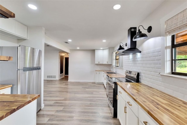 kitchen featuring wall chimney exhaust hood, a sink, visible vents, butcher block countertops, and appliances with stainless steel finishes