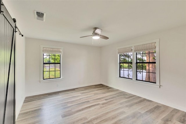 empty room with a barn door, visible vents, light wood-style floors, baseboards, and ceiling fan