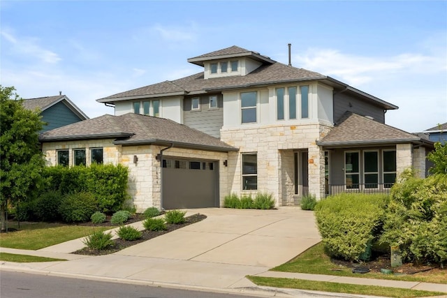 prairie-style house featuring a garage, roof with shingles, stone siding, and concrete driveway