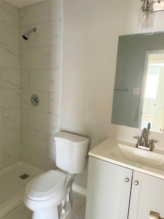 full bathroom with a tile shower, toilet, vanity, and baseboards