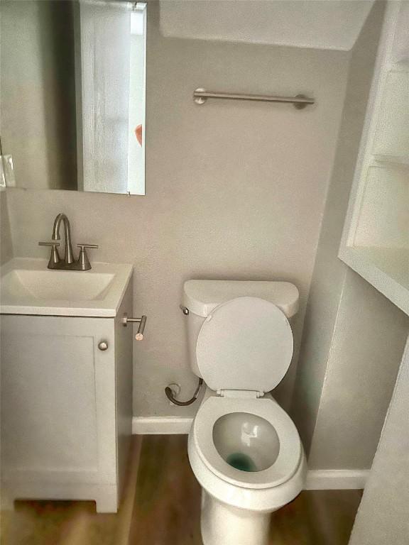 half bathroom with wood finished floors, vanity, toilet, and baseboards