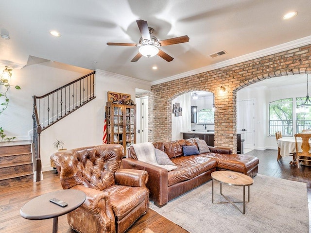 living area with arched walkways, visible vents, brick wall, stairway, and ceiling fan