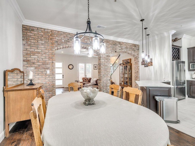 dining room featuring wood finished floors, arched walkways, crown molding, a chandelier, and brick wall