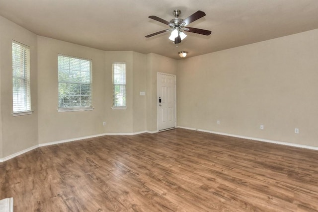 empty room with wood finished floors, a ceiling fan, and baseboards