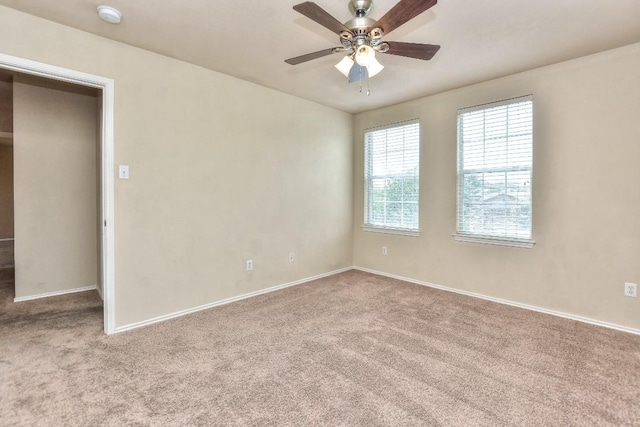 carpeted spare room with a ceiling fan and baseboards