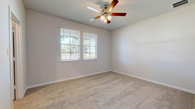 carpeted spare room with baseboards, a ceiling fan, and visible vents