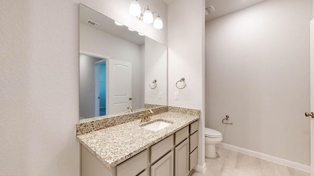 bathroom featuring toilet, vanity, visible vents, and baseboards