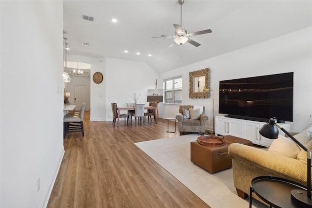 living room with vaulted ceiling, wood finished floors, ceiling fan with notable chandelier, baseboards, and visible vents