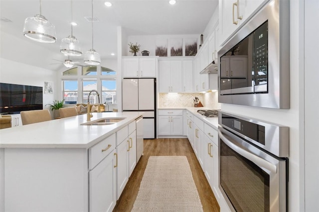 kitchen with stainless steel appliances, wood finished floors, a ceiling fan, a sink, and white cabinetry