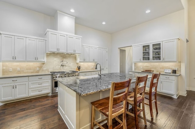 kitchen featuring a kitchen breakfast bar, a sink, tasteful backsplash, glass insert cabinets, and high end range