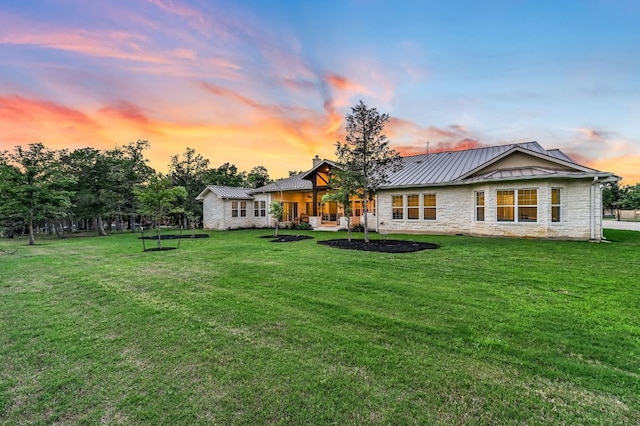 back of property at dusk with stone siding, a standing seam roof, a chimney, and metal roof