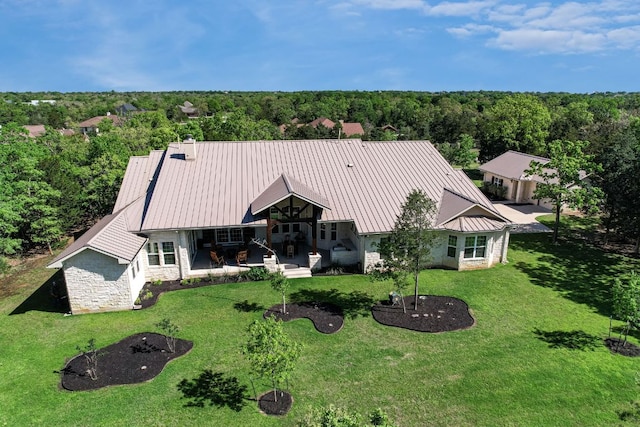 back of house with a yard, a forest view, stone siding, and metal roof