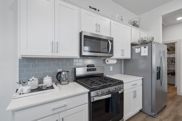 kitchen with backsplash, wood finished floors, appliances with stainless steel finishes, and white cabinetry