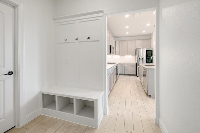 mudroom with recessed lighting, light wood-style flooring, baseboards, and a sink