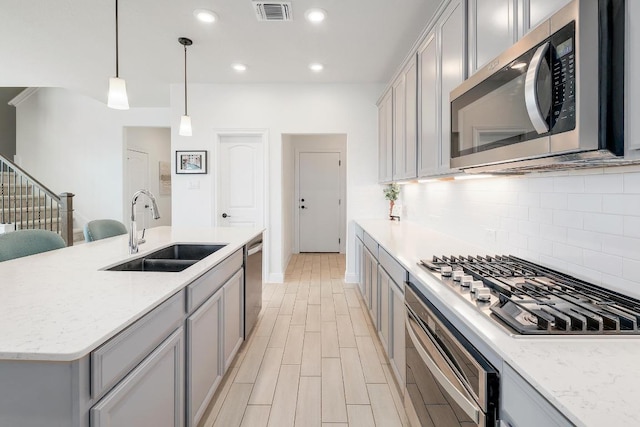 kitchen featuring stainless steel appliances, a sink, visible vents, backsplash, and gray cabinetry