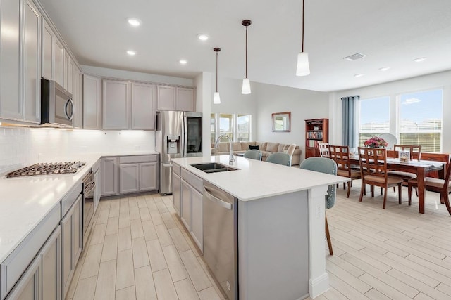 kitchen featuring a sink, tasteful backsplash, gray cabinets, light countertops, and appliances with stainless steel finishes