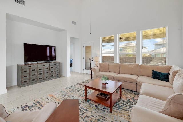 living room with a high ceiling, baseboards, wood finished floors, and visible vents