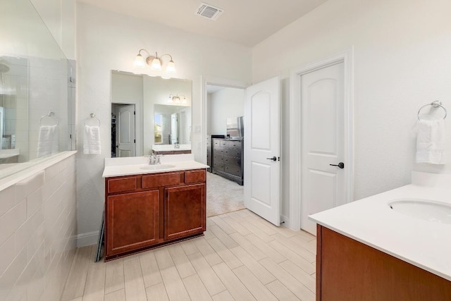 full bathroom with two vanities, a sink, visible vents, and tiled shower
