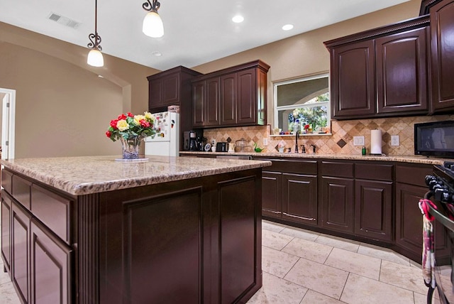316 County Rd, Bastrop, TX 78602 - kitchen featuring freestanding refrigerator, backsplash, light stone counters, decorative light fixtures, and dark brown cabinetry