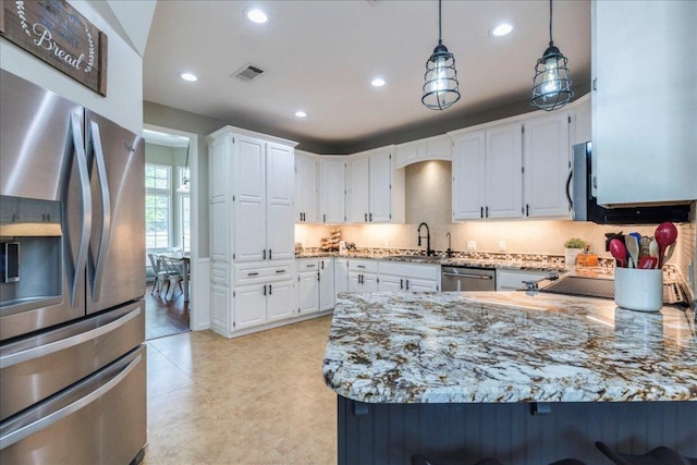 kitchen with white cabinets, appliances with stainless steel finishes, light stone countertops, and a sink