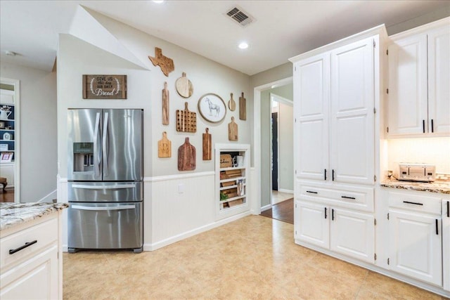 kitchen featuring white cabinetry, stainless steel fridge with ice dispenser, light stone counters, and visible vents