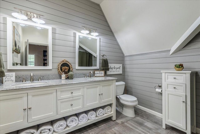 full bath with vaulted ceiling, toilet, wood walls, and a sink