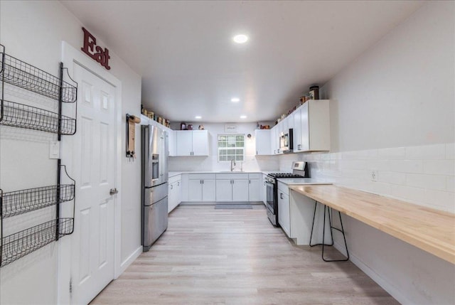 kitchen with recessed lighting, light wood finished floors, a sink, appliances with stainless steel finishes, and white cabinetry