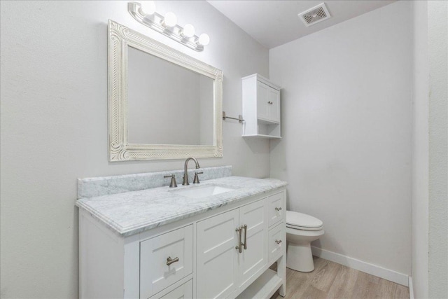 bathroom with wood finished floors, vanity, baseboards, toilet, and visible vents