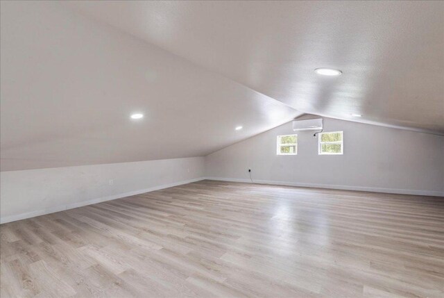additional living space with light wood-style flooring, a wall unit AC, vaulted ceiling, baseboards, and recessed lighting