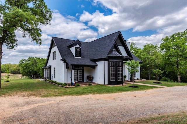 tudor home featuring roof with shingles, dirt driveway, and a front yard