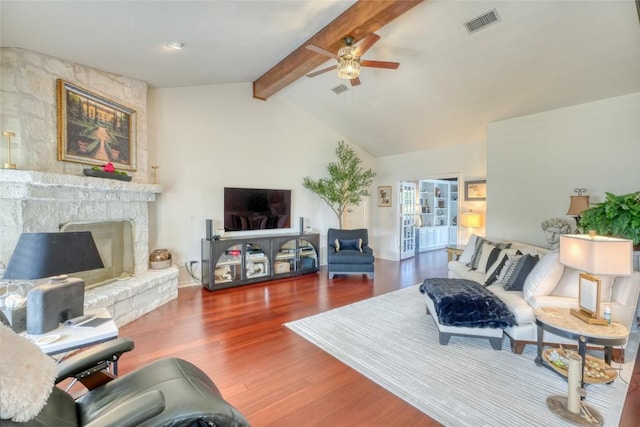 living area featuring wood finished floors, vaulted ceiling with beams, ceiling fan, a fireplace, and visible vents