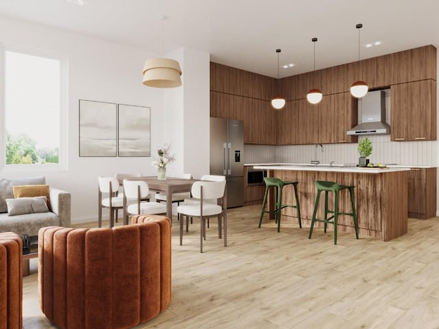 interior space with brown cabinets, stainless steel fridge, wall chimney exhaust hood, and modern cabinets