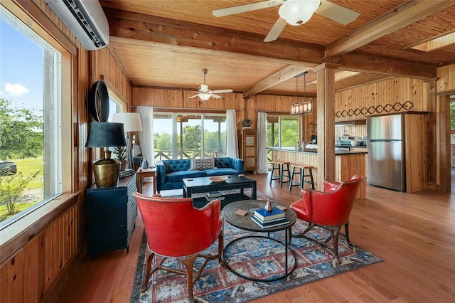 living area with a wall mounted air conditioner, ceiling fan, light wood-style flooring, wood walls, and beam ceiling