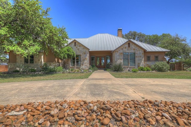 ranch-style home featuring a chimney, stone siding, french doors, fence, and metal roof