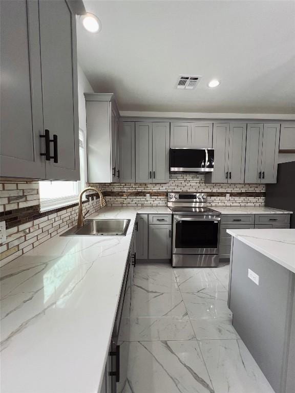kitchen with backsplash, visible vents, gray cabinets, a sink, and appliances with stainless steel finishes