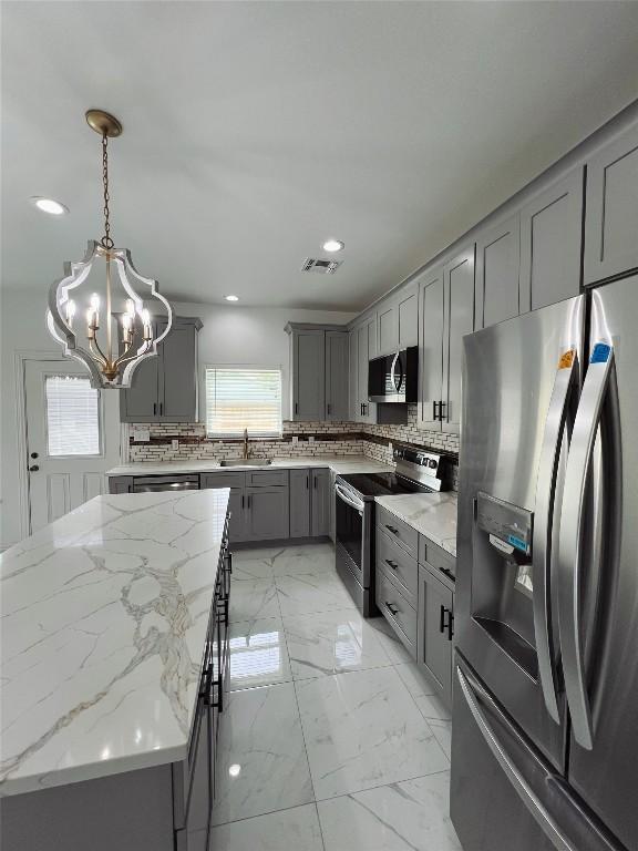 kitchen with gray cabinets, appliances with stainless steel finishes, a notable chandelier, and tasteful backsplash