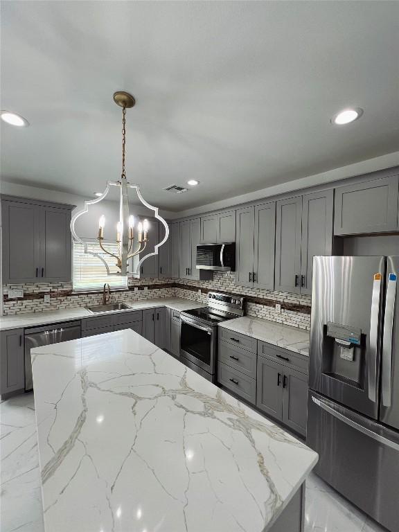 kitchen featuring a sink, a notable chandelier, decorative backsplash, gray cabinets, and appliances with stainless steel finishes