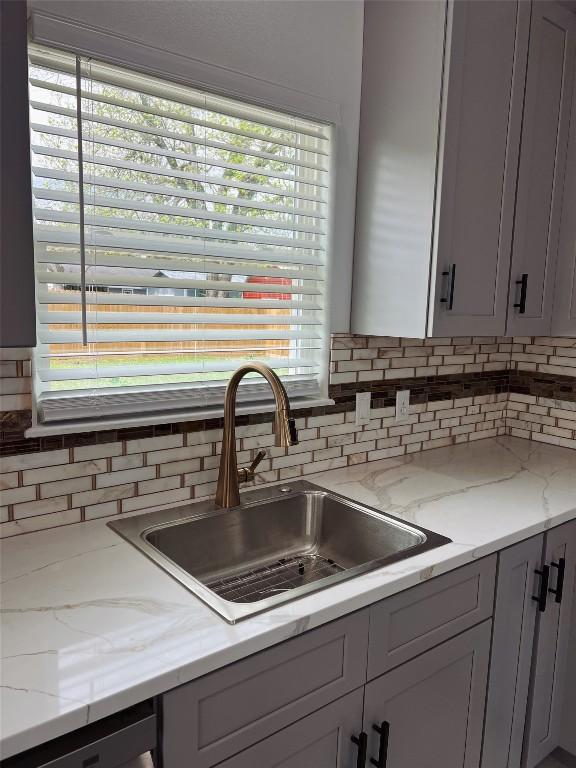 kitchen featuring light stone countertops, dishwashing machine, decorative backsplash, and a sink