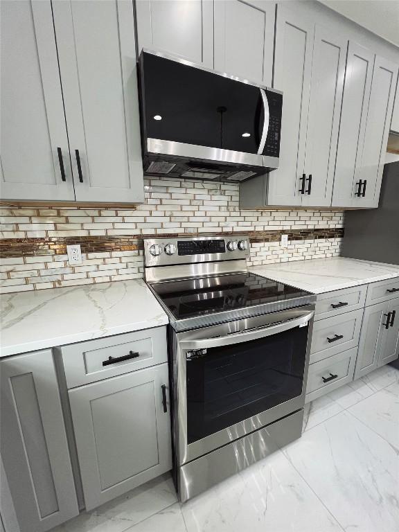 kitchen featuring marble finish floor, light stone counters, stainless steel appliances, gray cabinets, and tasteful backsplash