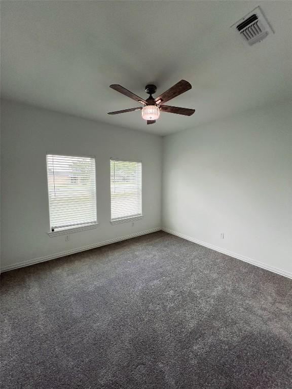 empty room with baseboards, visible vents, dark carpet, and ceiling fan