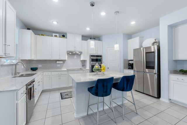 245 Six Shooter Dr, Kyle, TX 78640 - kitchen featuring appliances with stainless steel finishes, a center island, tasteful backsplash, light stone counters, and white cabinetry