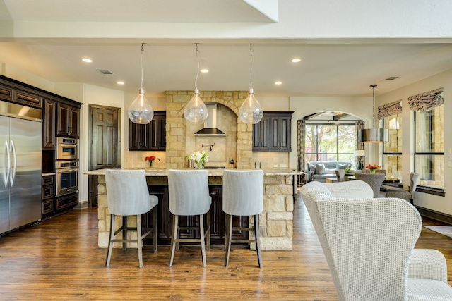 2104 University Club Dr, Austin, TX 78732 - kitchen with appliances with stainless steel finishes, dark brown cabinetry, arched walkways, decorative backsplash, and wall chimney exhaust hood