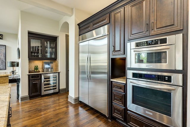 2104 University Club Dr, Austin, TX 78732 - kitchen featuring appliances with stainless steel finishes, wine cooler, dark brown cabinetry, arched walkways, and dark wood-style flooring