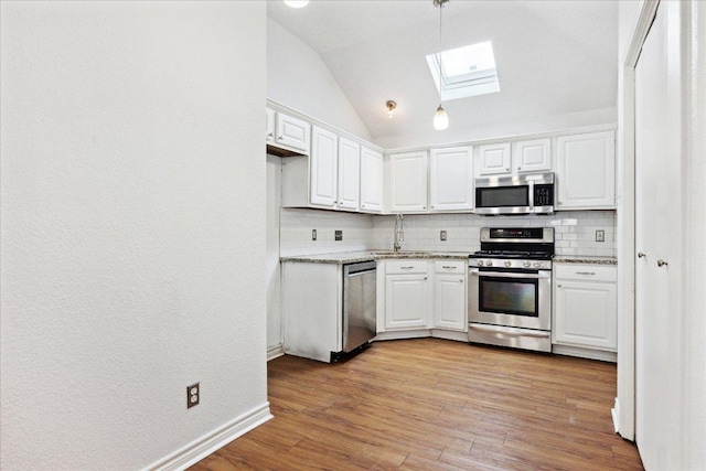 kitchen with lofted ceiling with skylight, decorative backsplash, white cabinetry, and stainless steel appliances